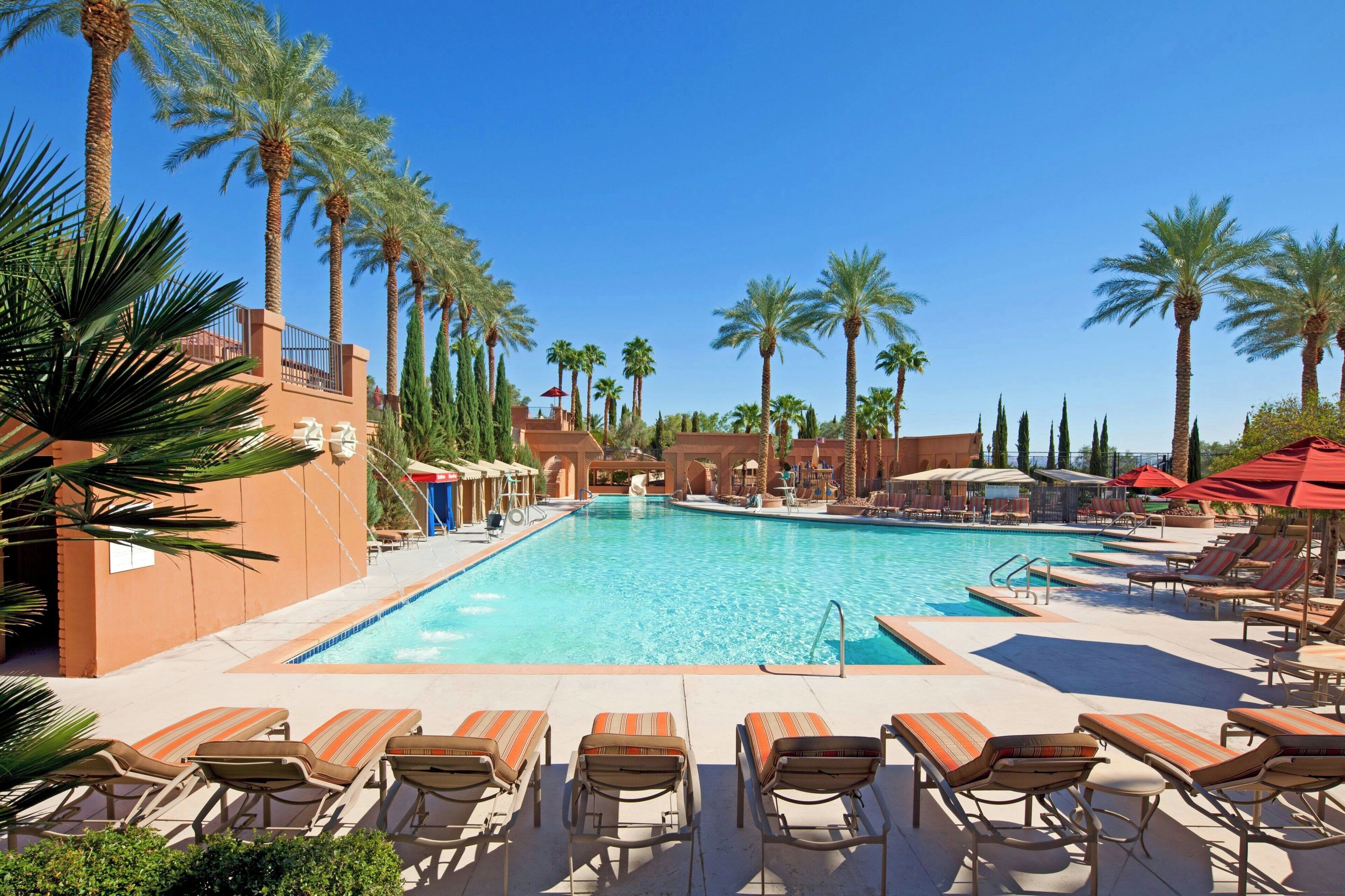 A pool area with lounge chairs and palm trees.