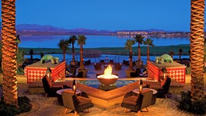 A lounge area with a fire pit, seating, and a view of a lake and mountains.