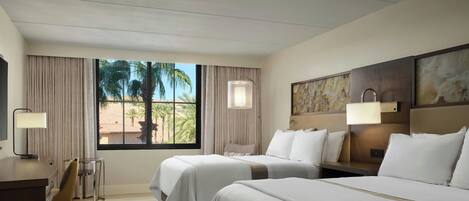 Habitación de hotel con dos camas, un escritorio, una silla, una mesita y una ventana con cortinas.