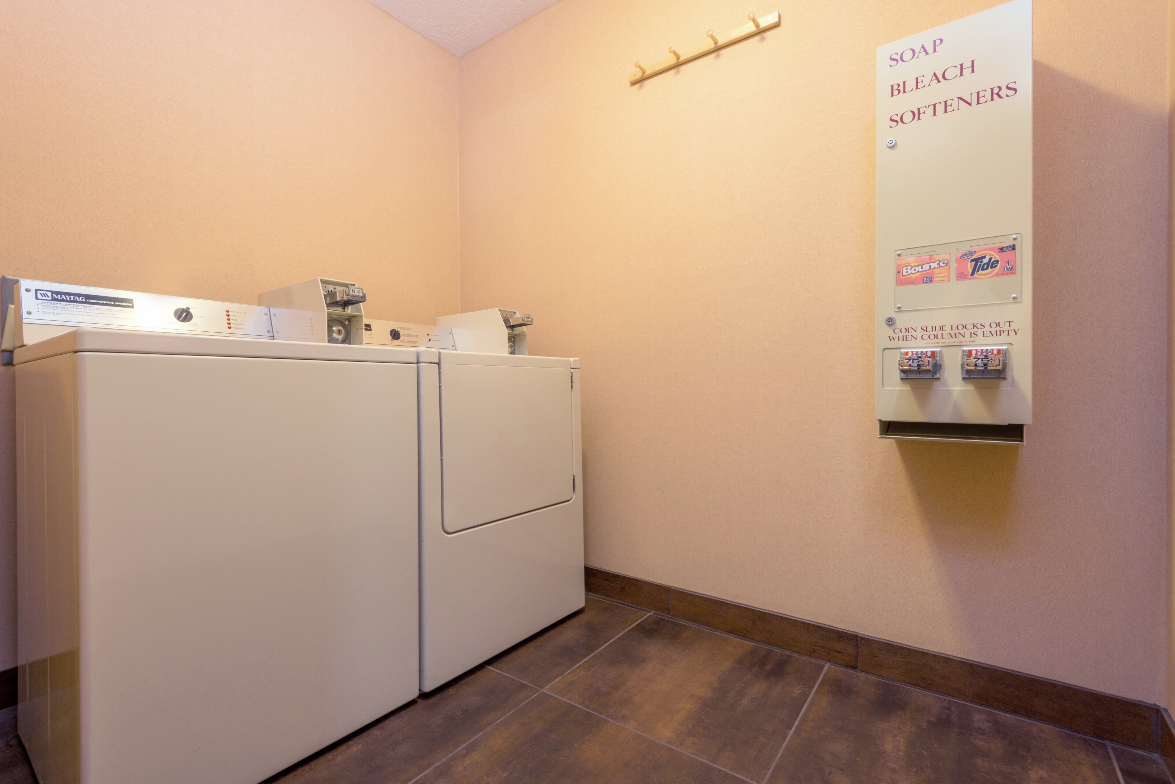 A laundry area with a Maytag washer and dryer, a soap and bleach softener dispenser, and a coin-operated laundry detergent dispenser.