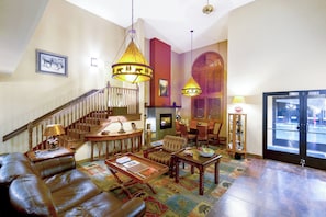 A spacious living area with a staircase, leather sofa, wooden coffee table, and a dining table with chairs.