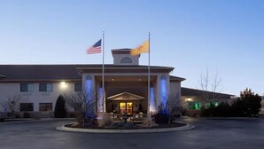 A hotel entrance with a flagpole, a covered entrance, and a landscaped area with trees and shrubs. - Holiday Inn Express Hotel & Suites Raton by IHG (Raton)