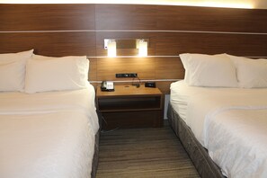 A hotel room with two beds, a nightstand with a phone and a clock, and a wooden headboard.
