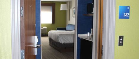 A hotel room with a bed, a desk, and a bathroom visible through an open door.