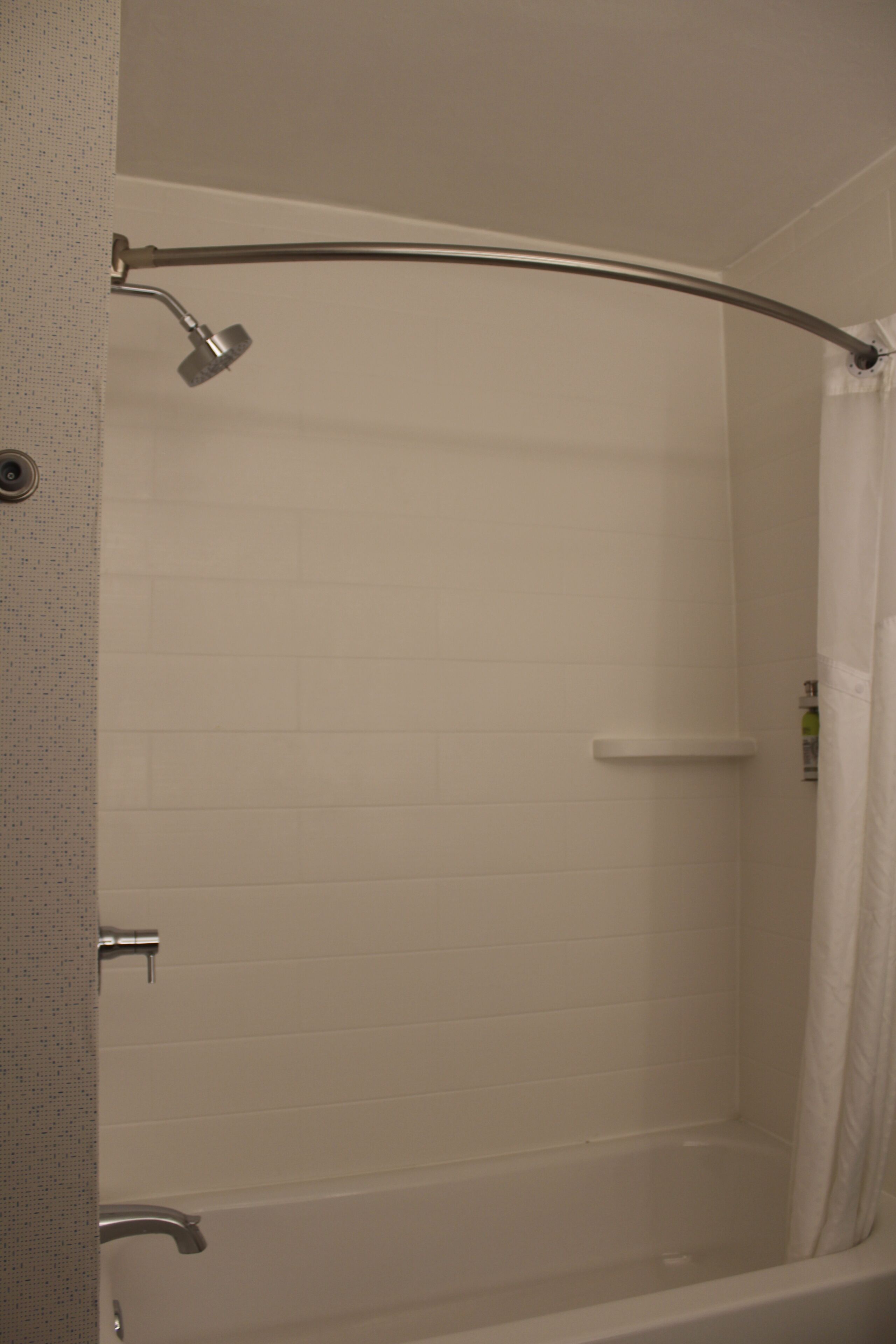 A white tiled shower with a curved showerhead and a white curtain.
