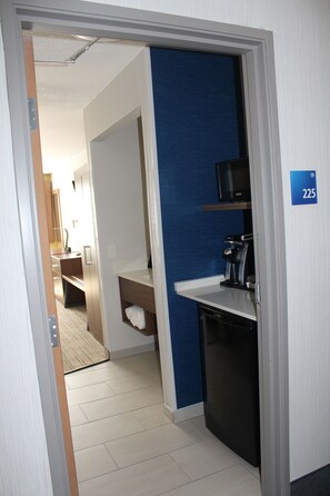 A hotel room with a kitchenette, a blue accent wall, and a door leading to a bathroom. - Holiday Inn Express Hotel & Suites Raton by IHG (Raton)