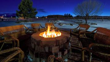 A fire pit surrounded by wicker chairs in a snowy outdoor setting at dusk.
