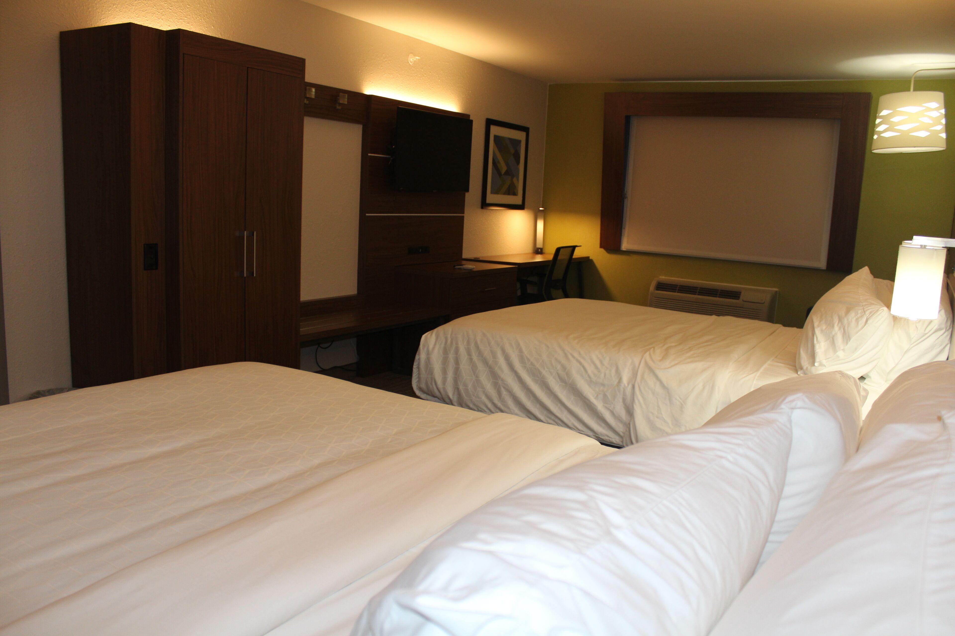 A hotel room with two beds, a desk, a television, and a window.