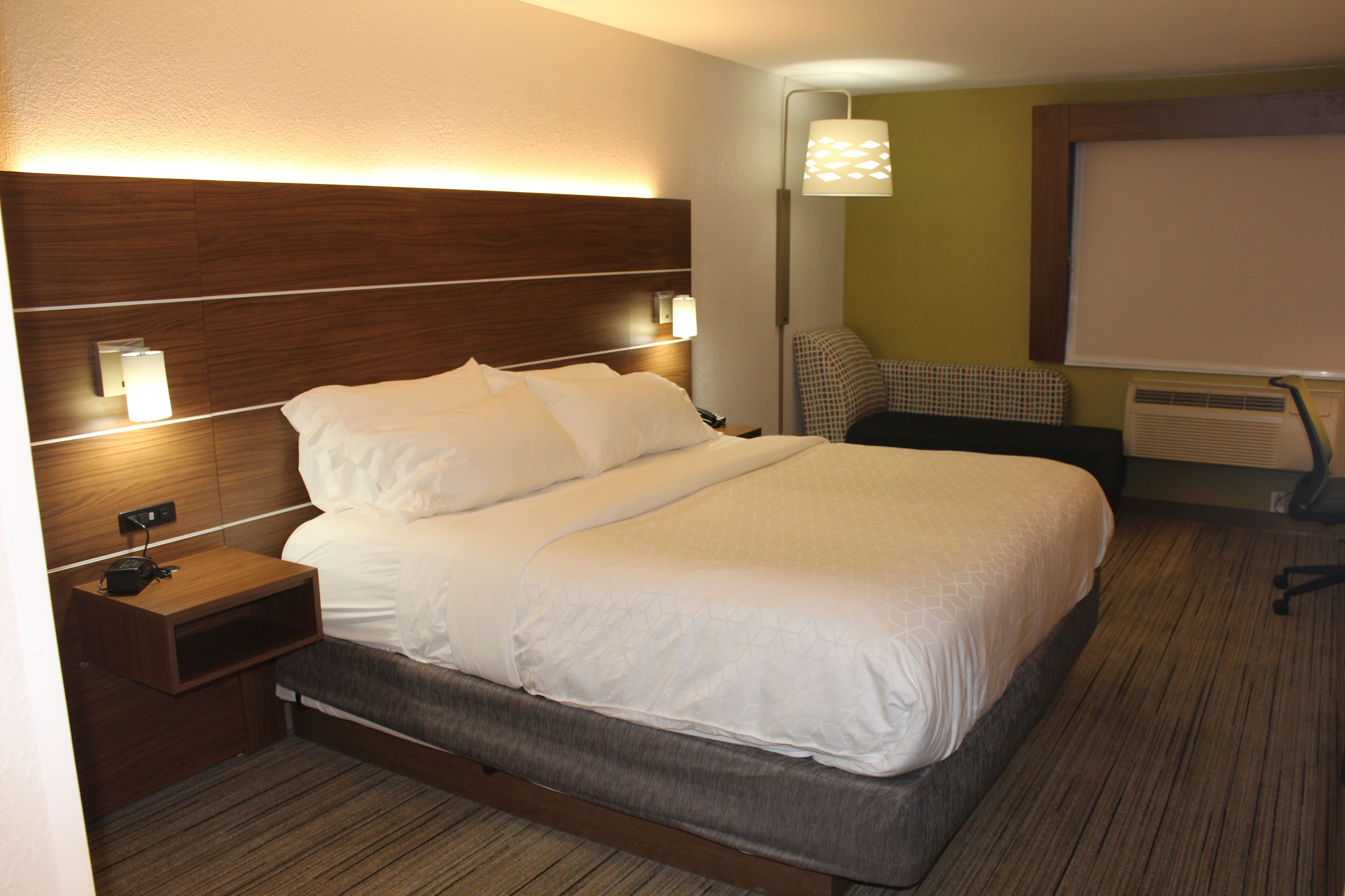 Une chambre d’hôtel avec un grand lit, des tables de chevet, une lampe, une chaise et un écran de projection.