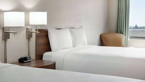 Habitación de hotel con dos camas, una mesita de noche, una lámpara y vistas de la ciudad.