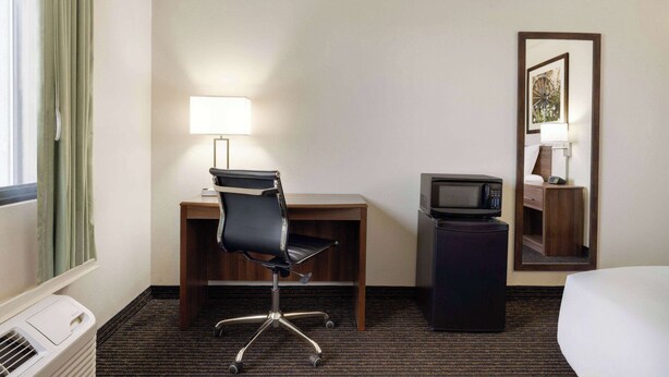 Een hotelkamer met een bureau, stoel, lamp, televisie en een bed.