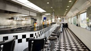 Een modern restaurant met een geruite vloer, barstoelen en een lange toonbank.