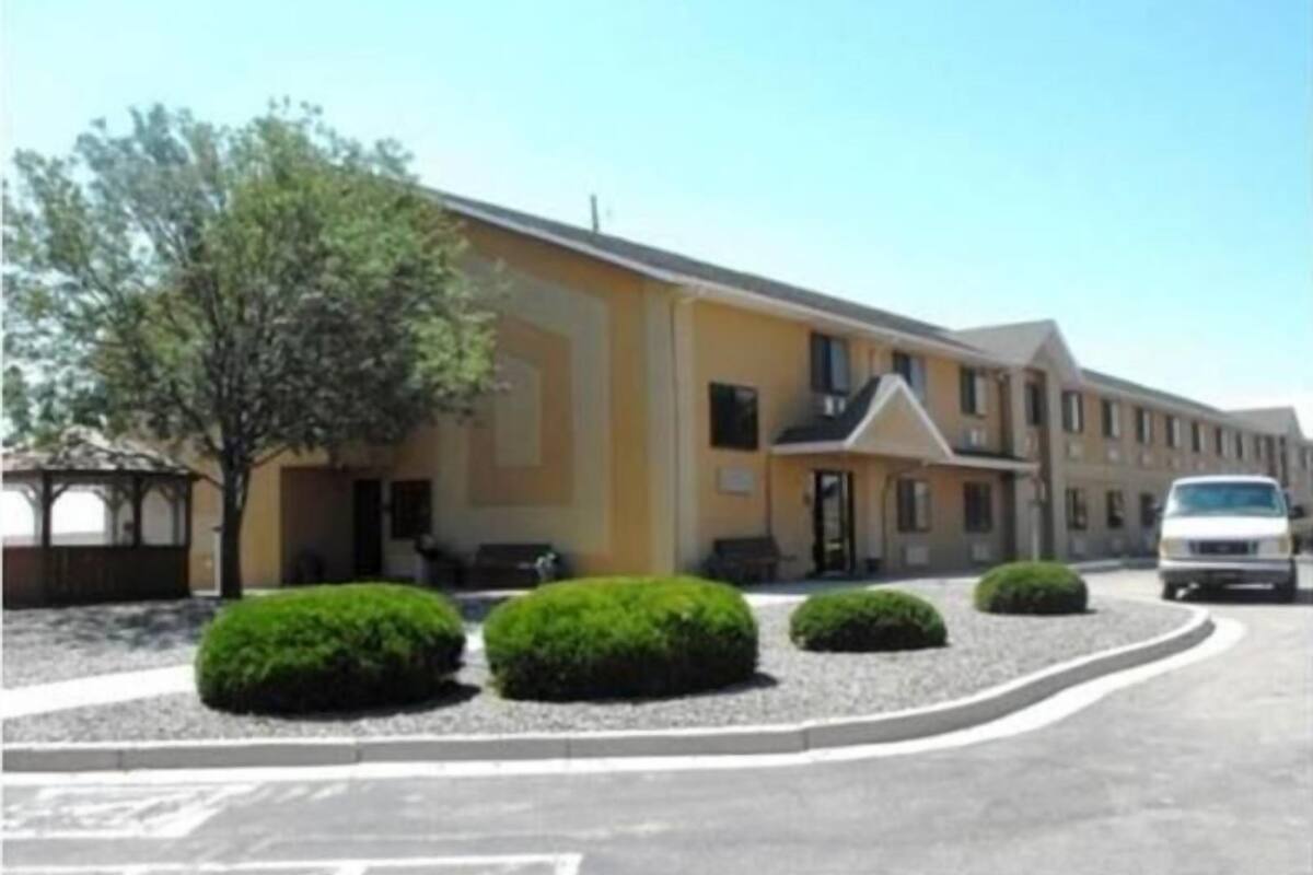 Un hôtel à plusieurs étages, doté d’une façade jaune, d’un parking où se trouve un fourgon blanc, et d’un aménagement paysager bien entretenu.