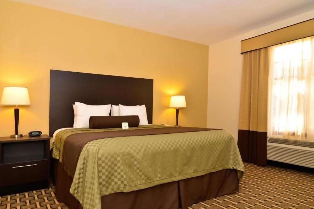 A hotel room with a bed, two bedside tables, lamps, a window with curtains, and a radiator.