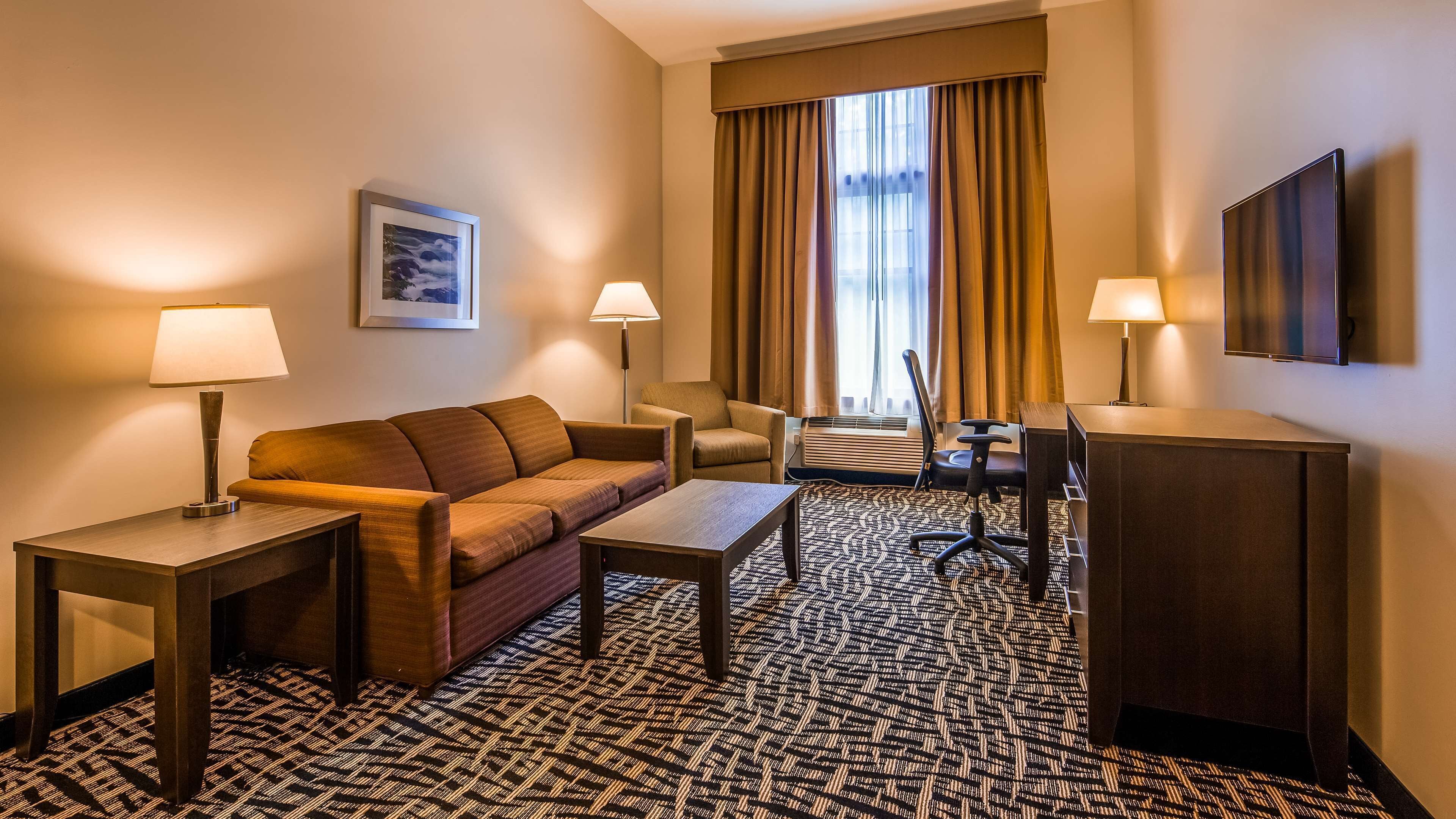 A hotel room with a sofa, two armchairs, a desk, and a flat-screen TV.
