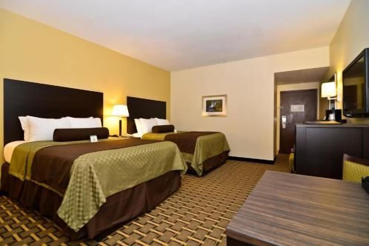 A hotel room with two beds, a desk, a television, and a door leading to a bathroom.