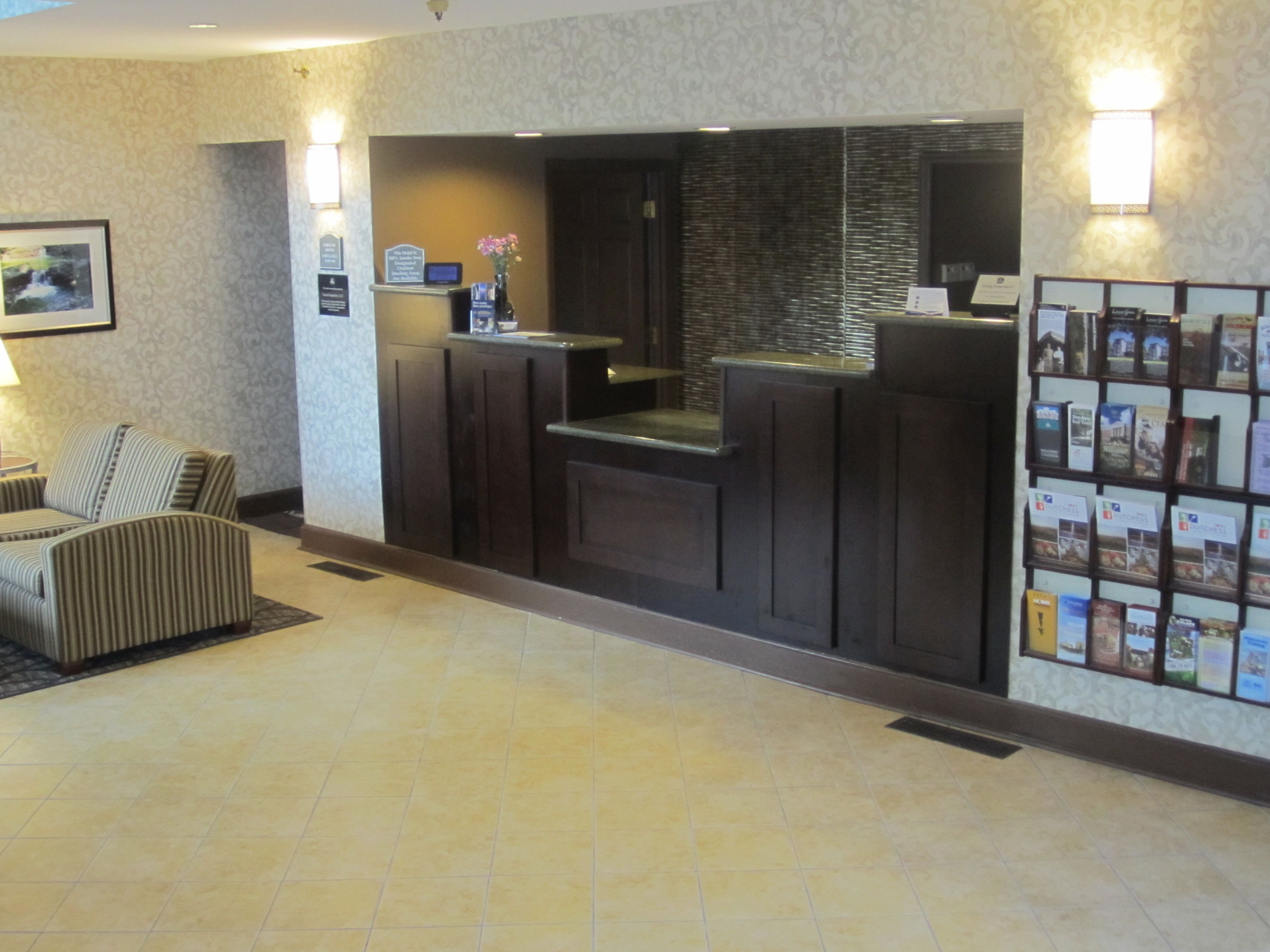 A reception area with a reception desk, a seating area with striped chairs, a tiled floor, and a wall with framed pictures and a bulletin board.