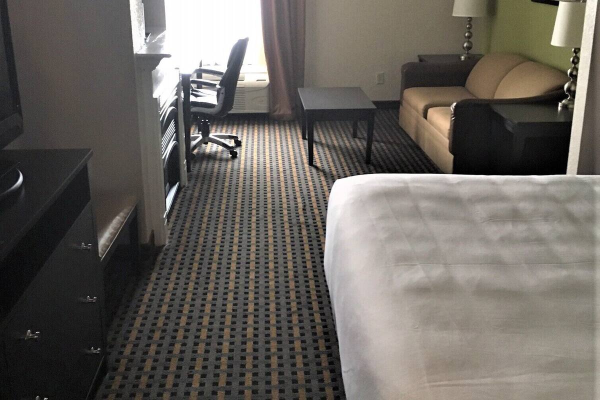 A hotel room with a bed, a desk, a chair, a television, a lamp, and a window with curtains.