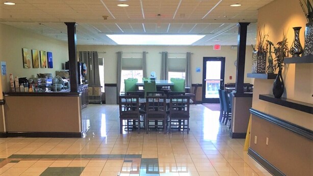 Un hall d’entrée spacieux, doté d’un sol carrelé, d’un comptoir de réception et d’un espace repas avec des tables et des chaises.