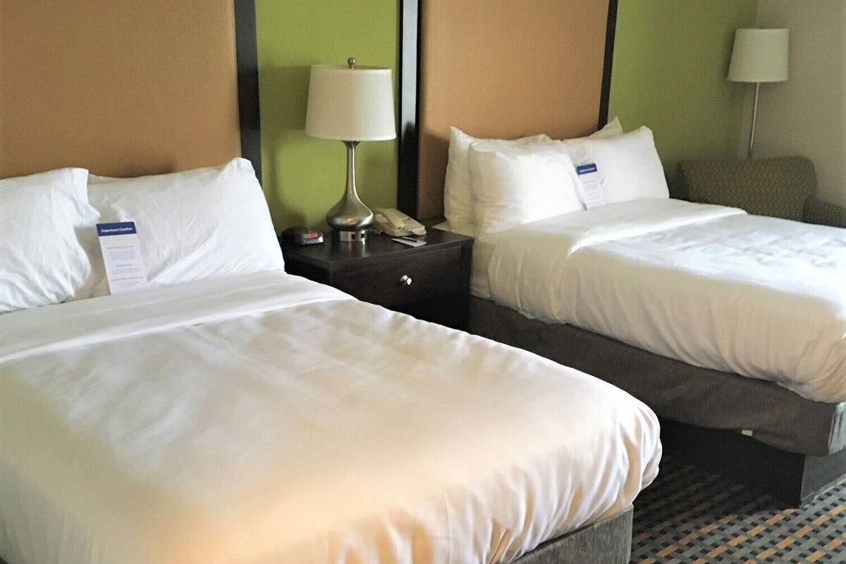 A hotel room with two beds, a nightstand with a lamp, and a chair.