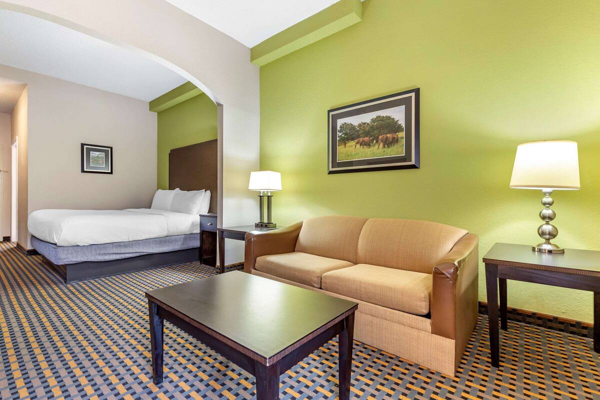 A hotel room with a bed, a sofa, a table, and a lamp.