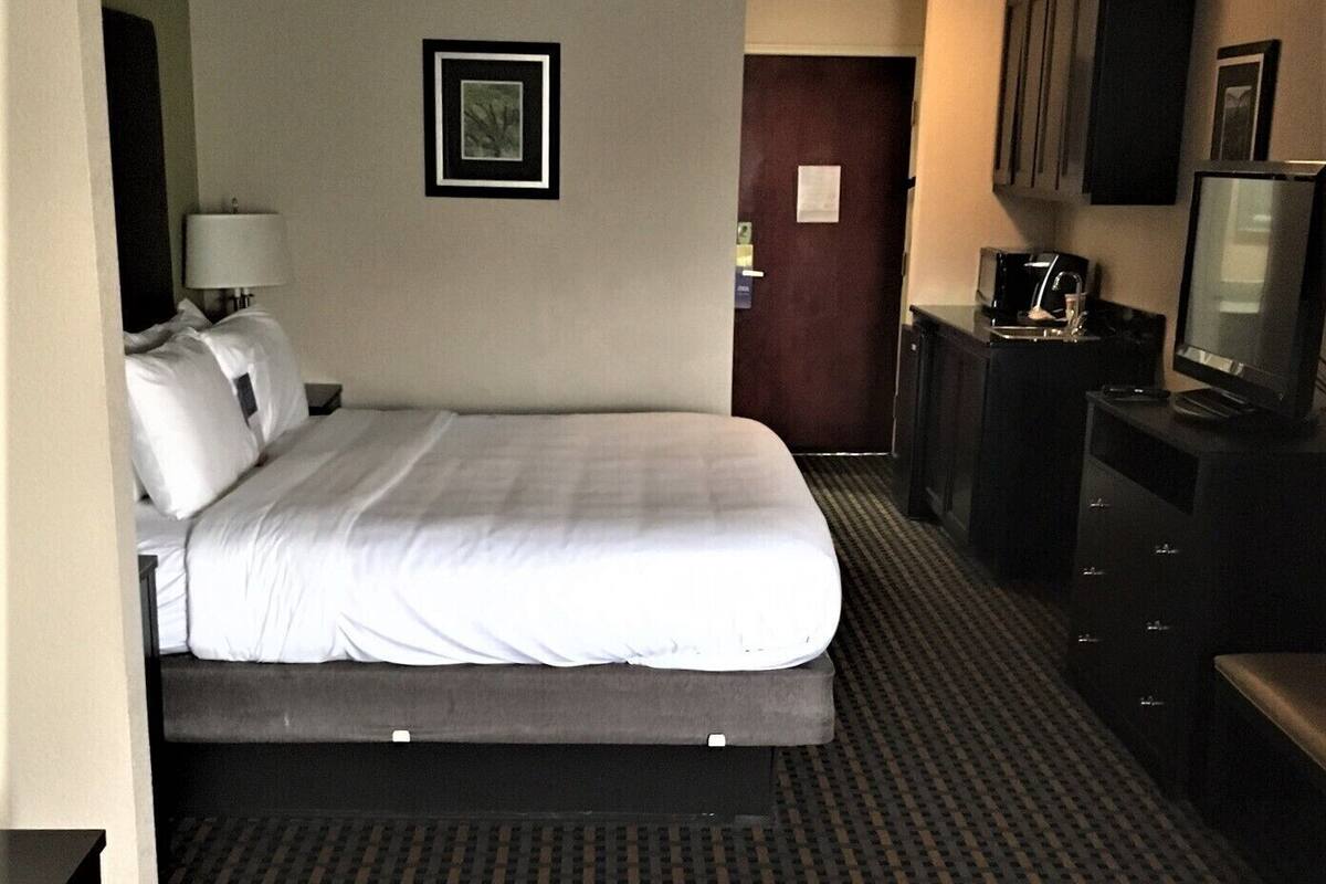 A hotel room with a bed, a desk with a computer, a TV, and a door.