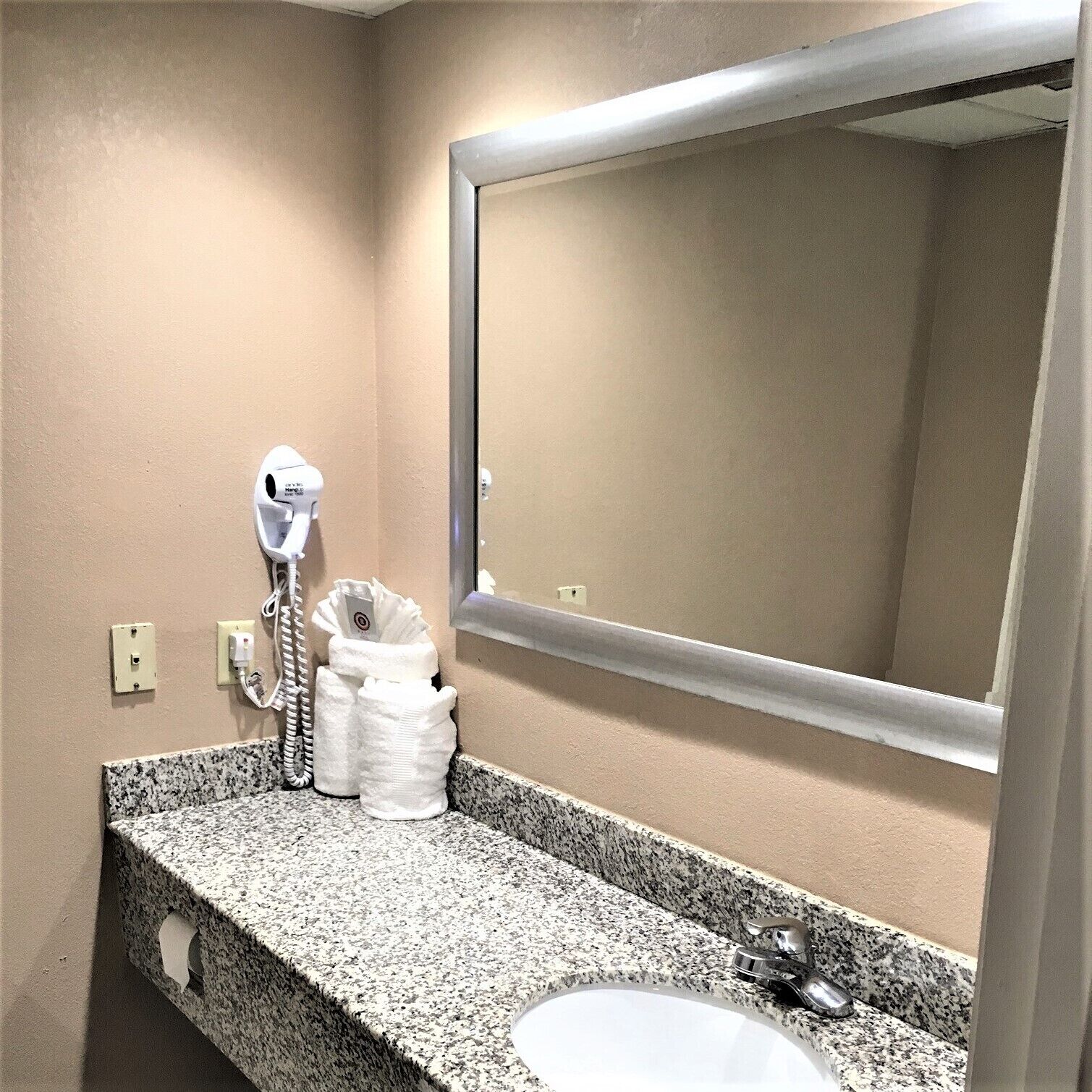A bathroom with a granite countertop, a sink, a mirror, and a hairdryer.