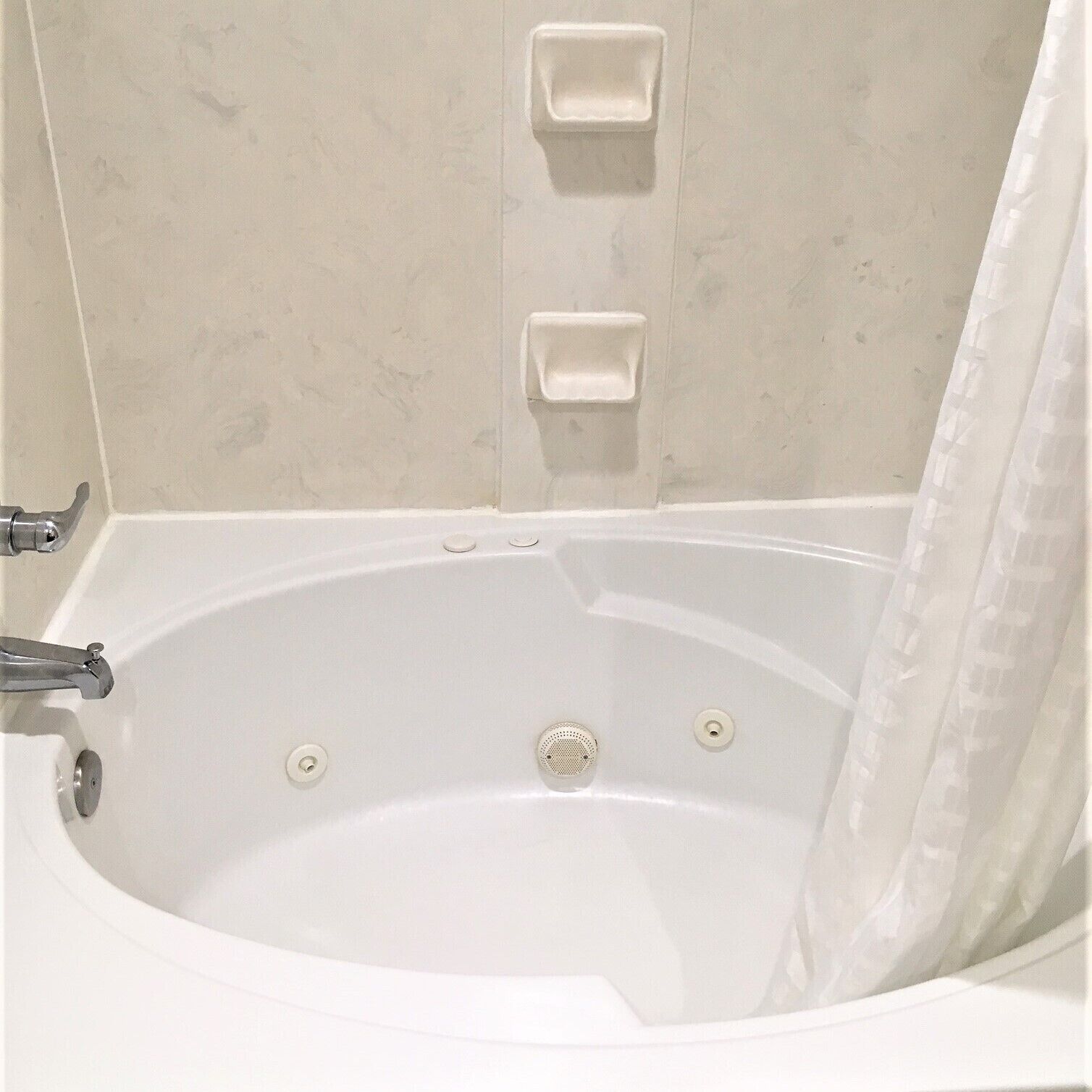 Una vasca da bagno bianca con tenda da doccia, un soffione manuale e due portasaponi a parete.