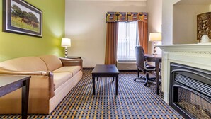 Une chambre d’hôtel avec un canapé, une petite table, une chaise, une cheminée et un tapis à motifs.