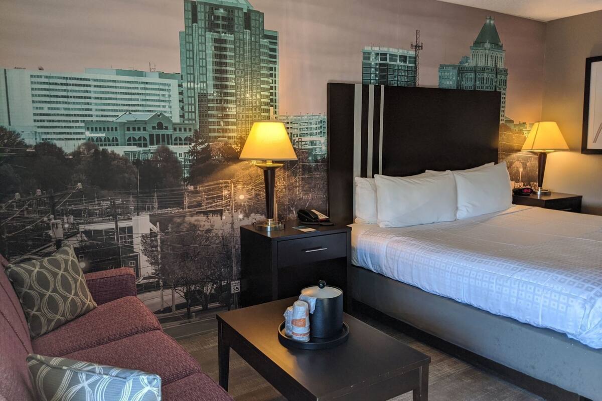 Une chambre d’hôtel comprenant un lit, deux tables de chevet, une table basse, un canapé et une fresque murale représentant un paysage urbain.