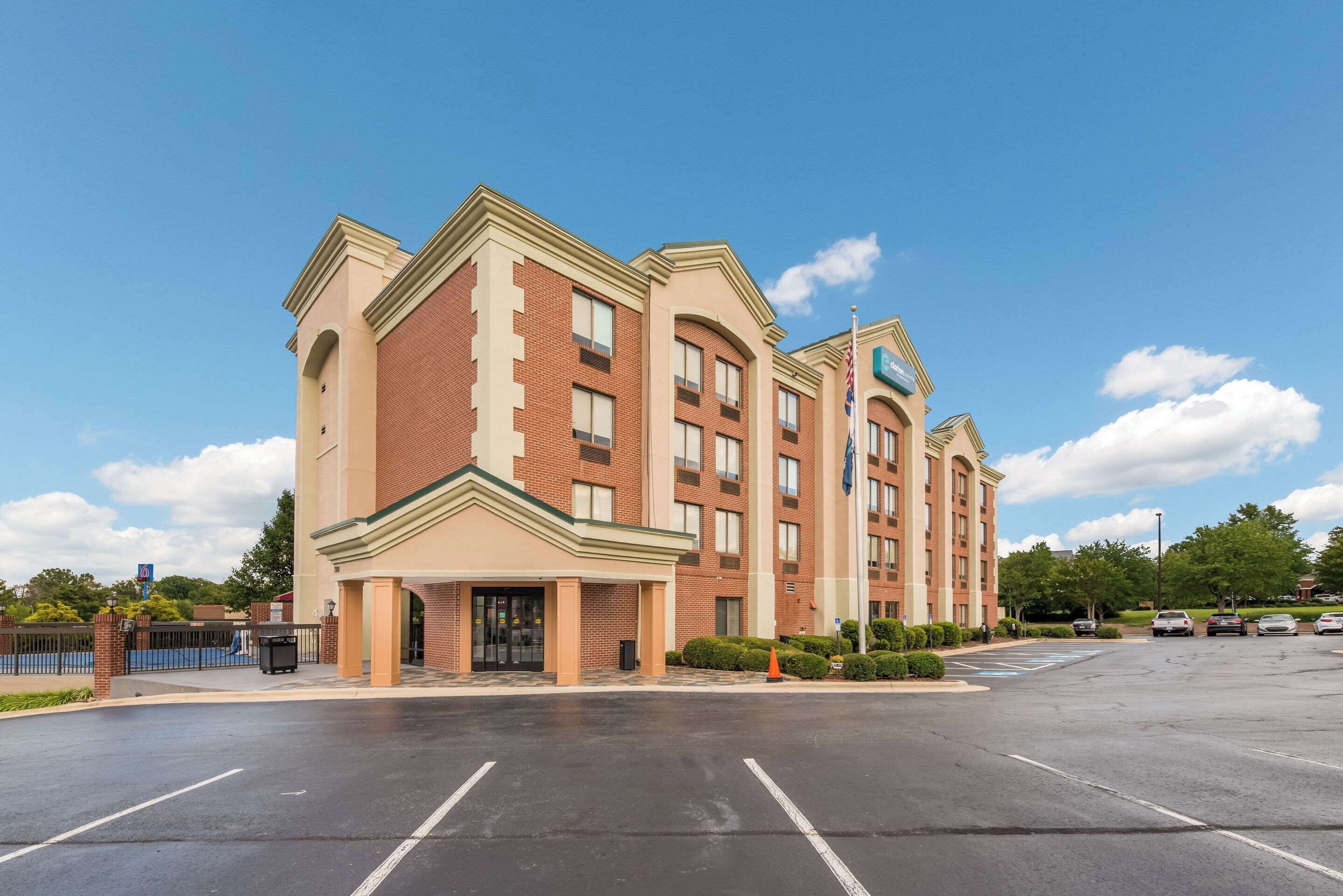 A multi-story hotel with a brick facade, a central entrance, and a parking lot in front.