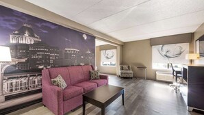 Un salon avec un canapé rouge, une table basse, un fauteuil à motifs et une grande fresque murale représentant un paysage urbain.