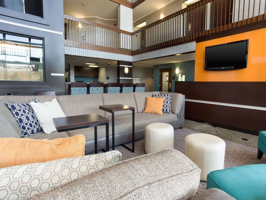 Een moderne lobby met een grijze bank, poefs, een kleine tafel en een aan de muur bevestigde televisie.