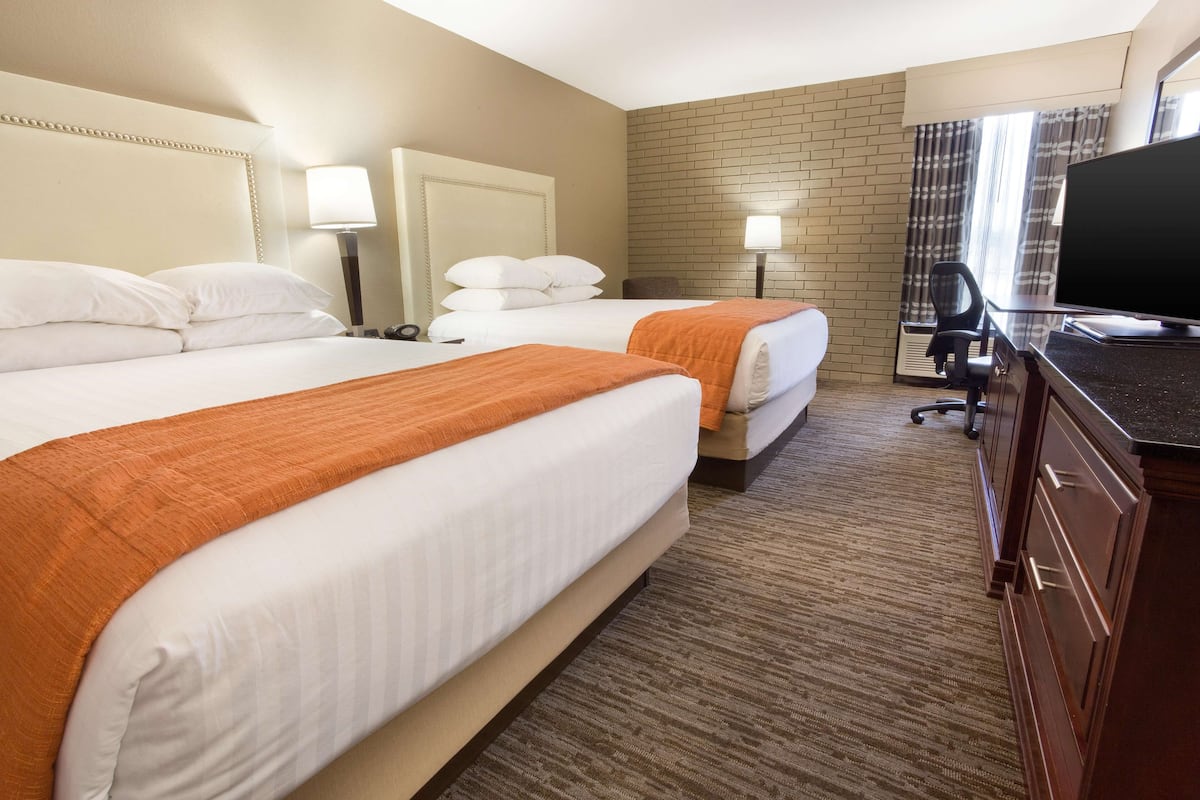 A hotel room with two beds, a desk, a television, and a brick-patterned wall.