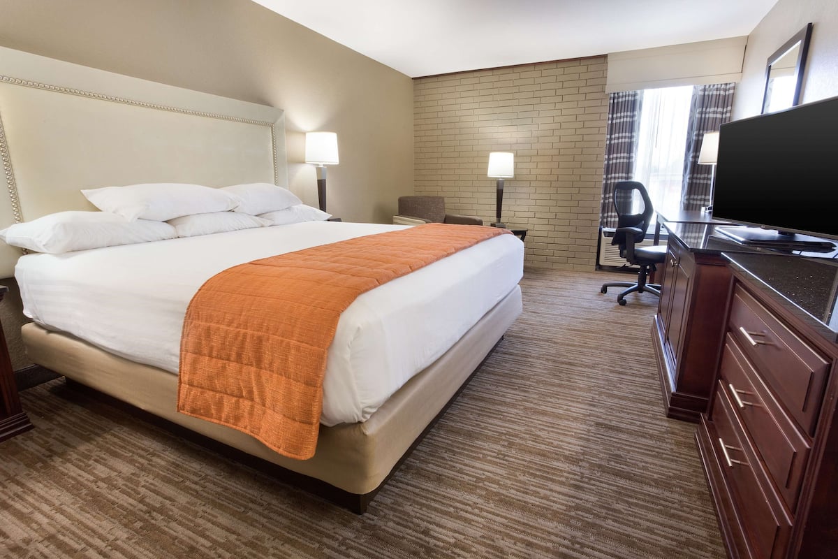 A hotel room with a large bed, a desk with a computer, a TV, and a window with curtains.