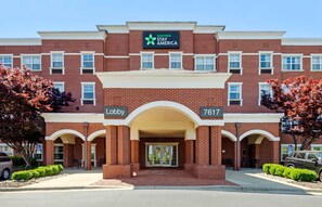 A brick building with a sign reading 'extended STAY AMERICA' and the number '7617' indicating the lobby. - Extended Stay America Suites Greensboro Airport (Greensboro)
