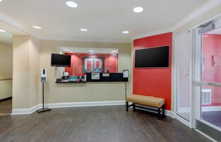 Zona de recepción con mostrador, banco, espejo grande y pared roja.