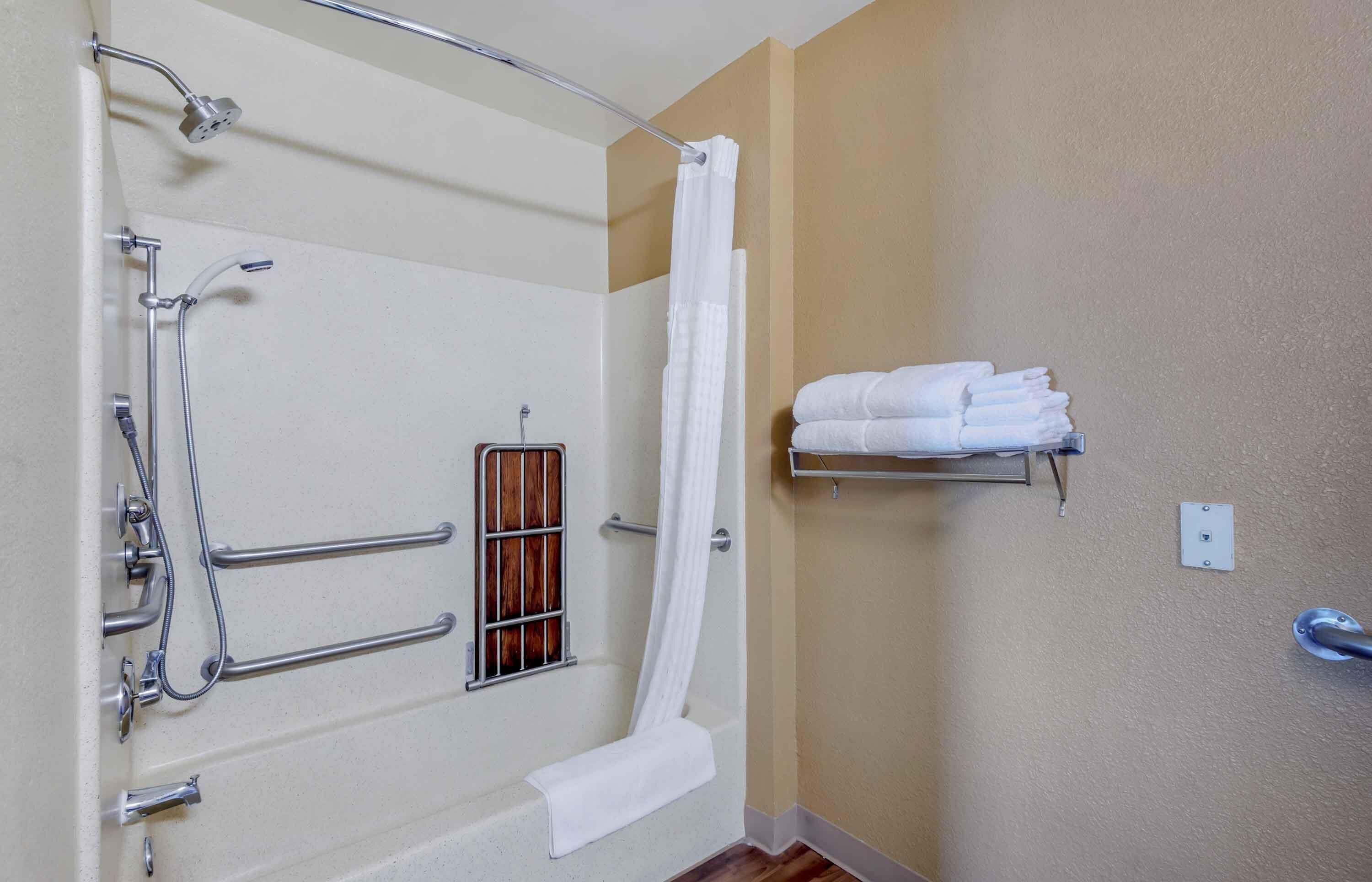 A bathroom with a bathtub, shower, and handrails.