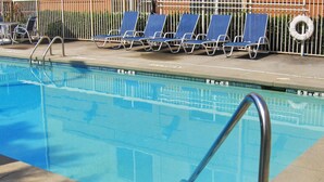 Una piscina con agua azul, una escalera metálica y varias sillas de descanso azules con estructura de metal.