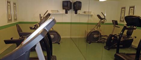 Un gimnasio con cintas de correr, bicicletas estáticas y una máquina de remo.