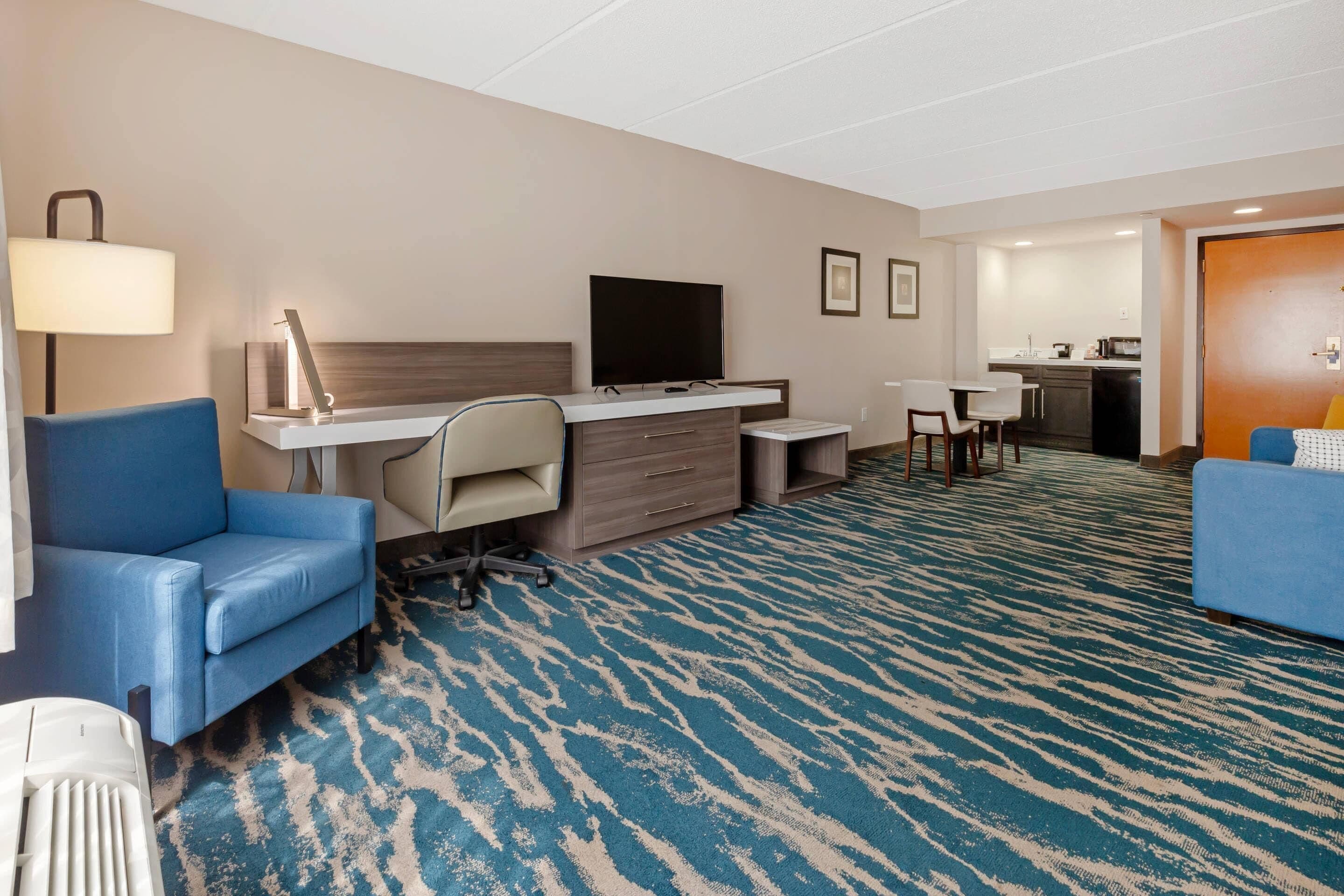 Une chambre d’hôtel équipée d’un bureau, d’une chaise, d’une télévision et d’un canapé bleu.