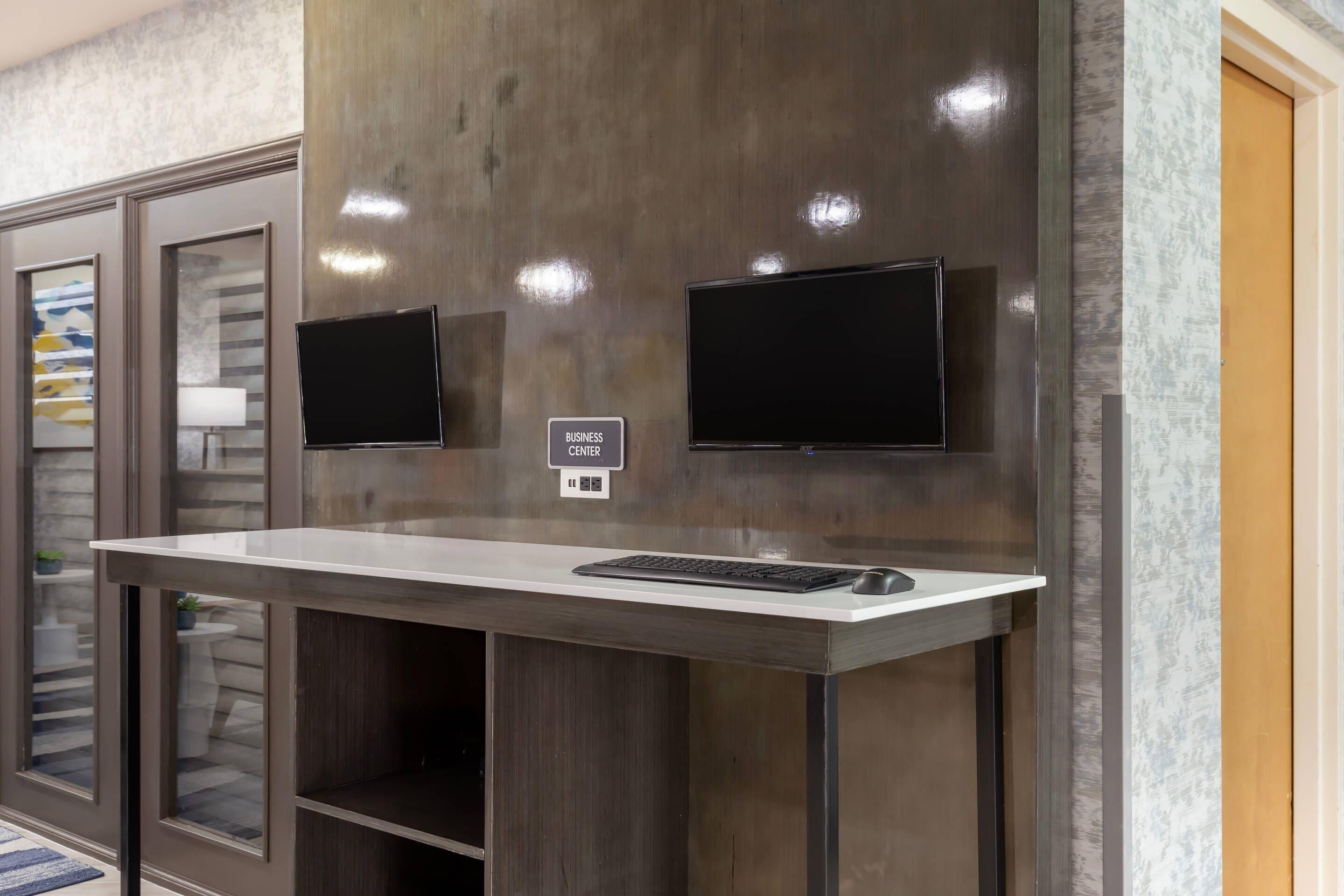 A business center with a desk, two monitors, and a sign indicating the location.