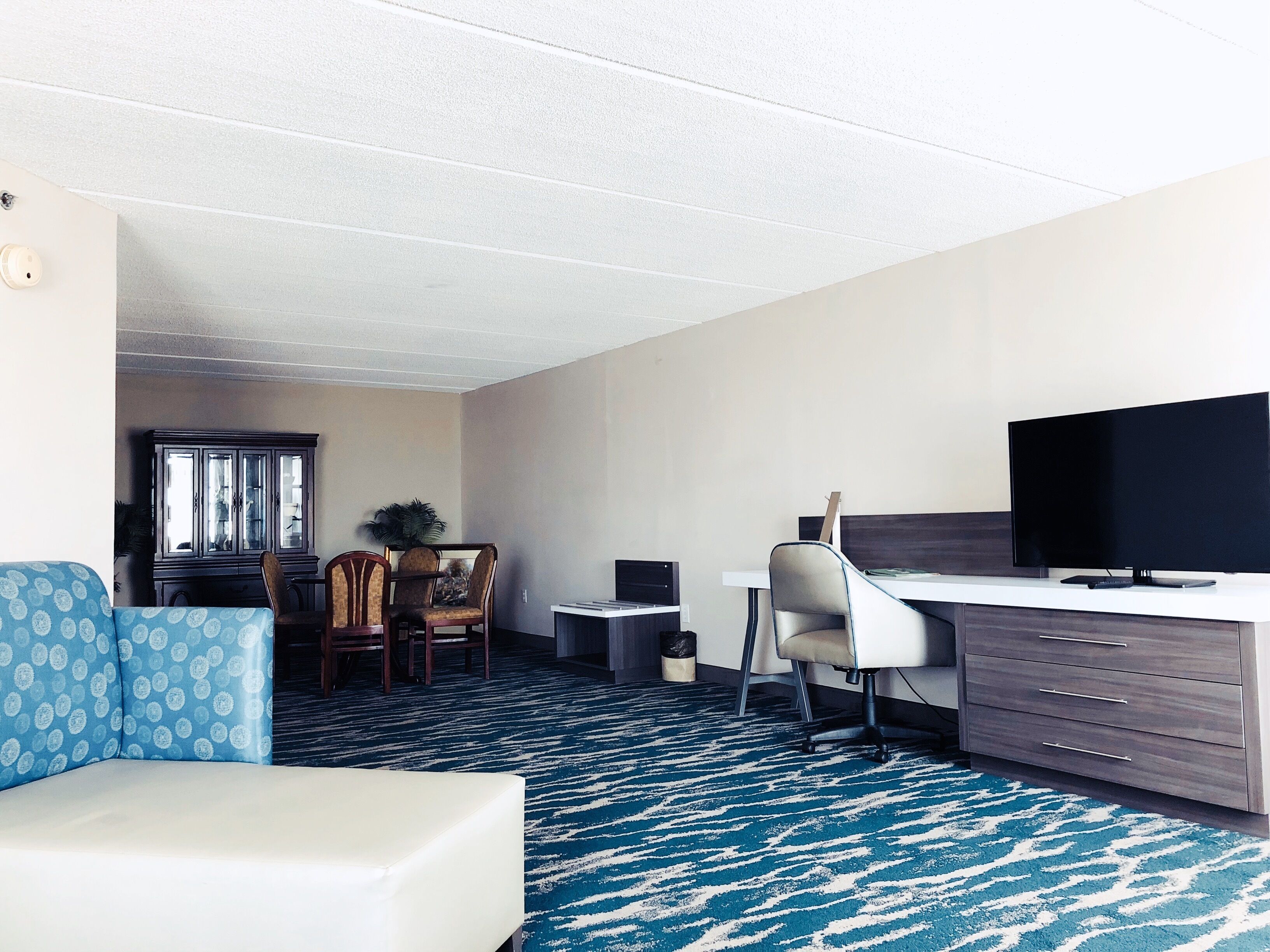 A hotel room with a bed, a desk, a TV, a chair, a dining table with chairs, and a window.