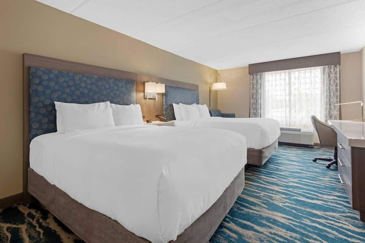 Une chambre d’hôtel avec deux lits, un bureau et une grande fenêtre.