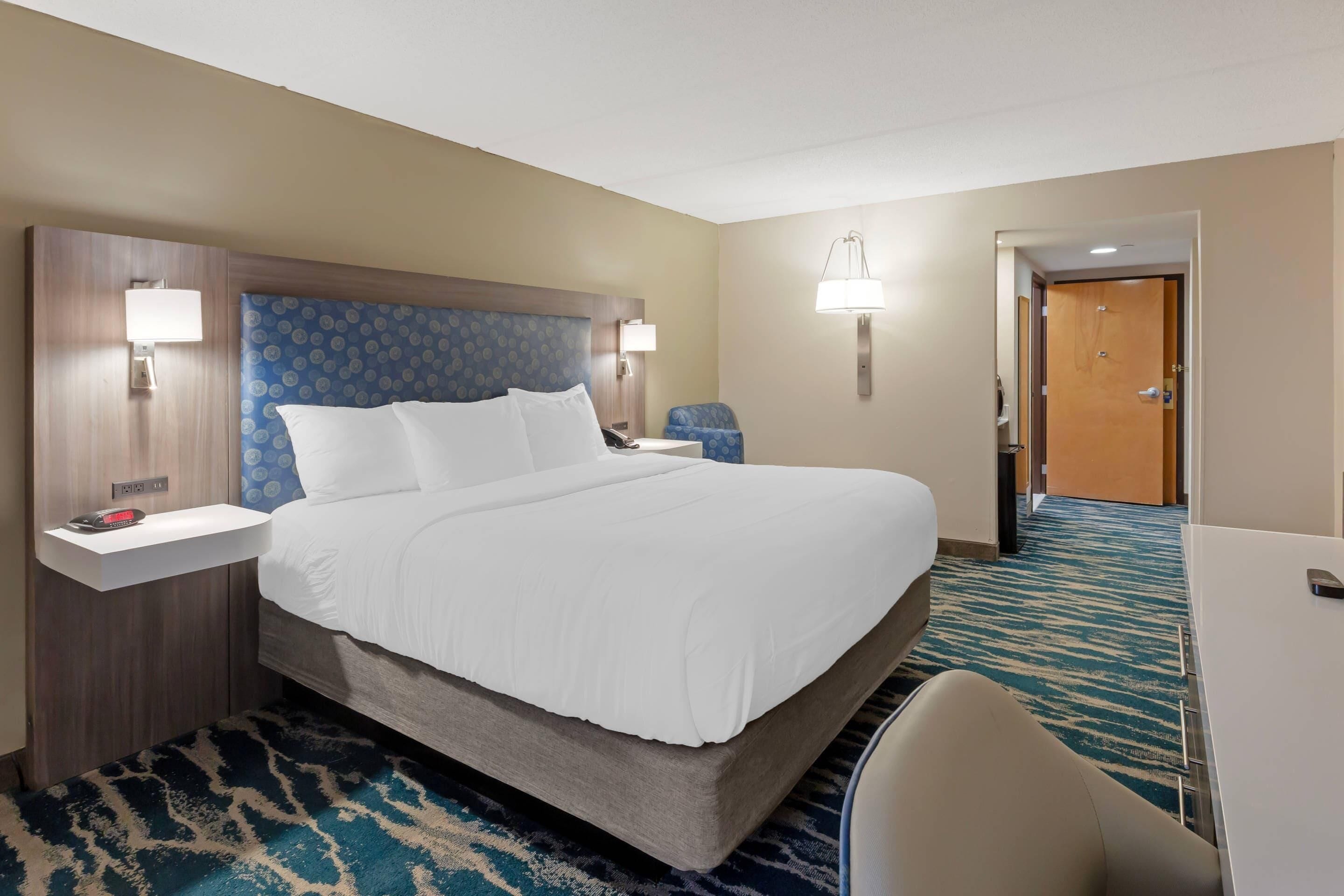 Ein Hotelzimmer mit einem großen Bett, Nachttischen, einem Schreibtisch und einem Sessel.