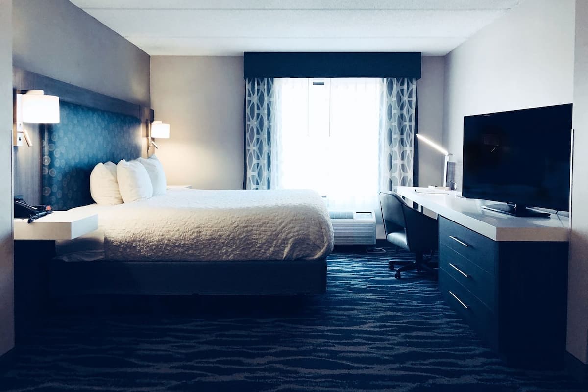 Une chambre d’hôtel avec un lit, un bureau, une télévision et une fenêtre avec des rideaux.