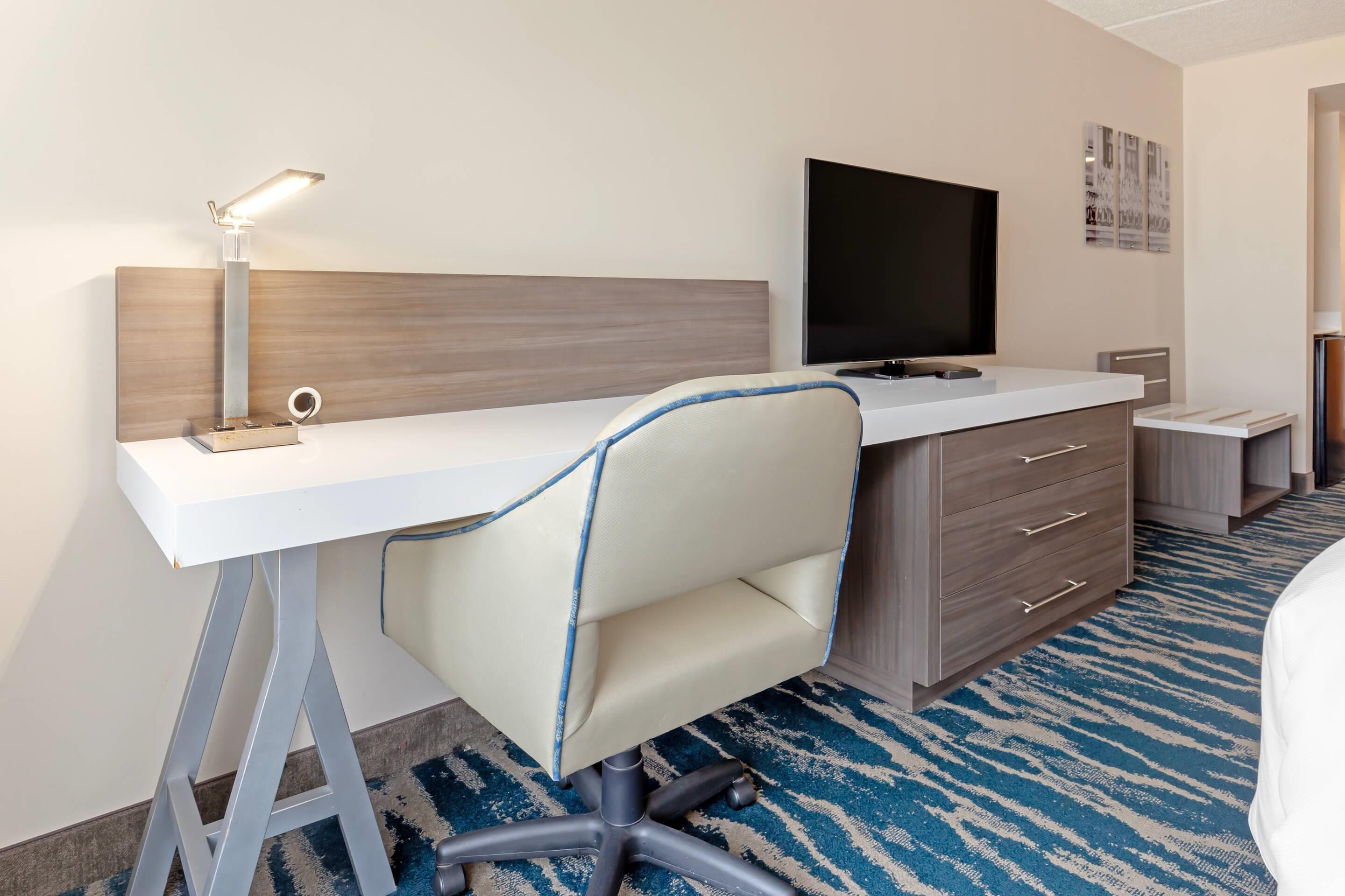 A hotel room with a desk, chair, television, and a bed.
