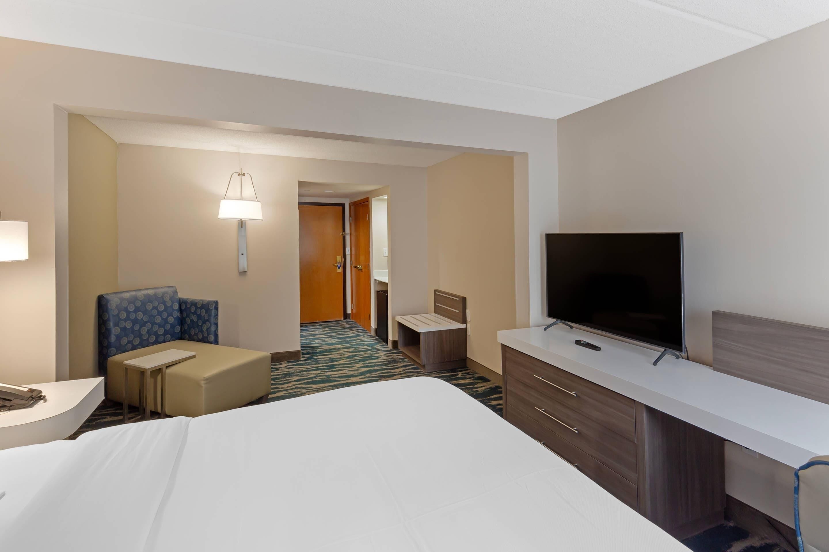 A hotel room with a bed, a desk, a television, and a seating area with a lamp.