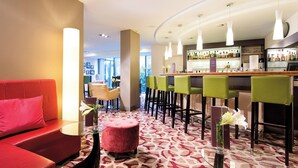 A modern hotel lobby with a red sofa, green bar stools, and a patterned carpet.