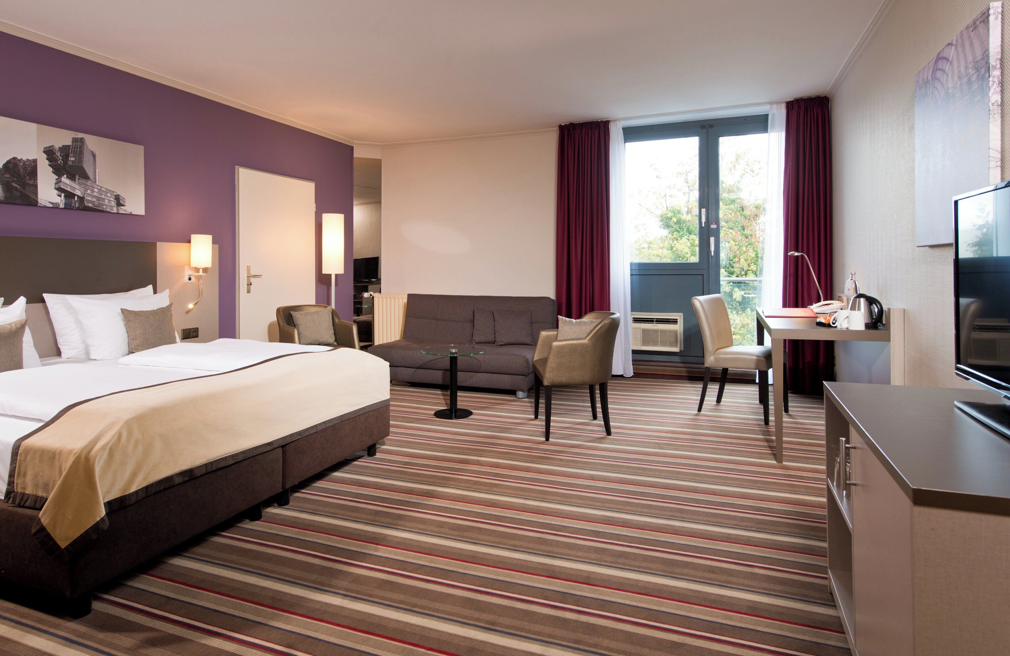 A hotel room with a bed, a sofa, a desk, and a TV.